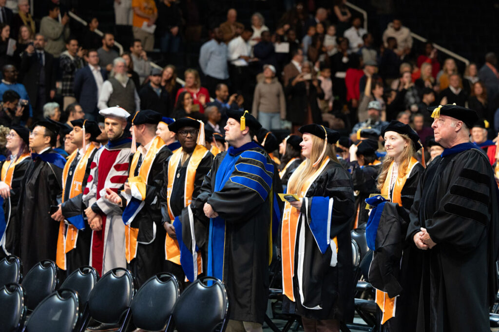 A group of faculty and doctoral candidates in regalia standing before the ceremony begins.