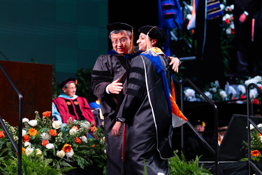 Hooded doctoral graduate and hooder preparing to walk off stage