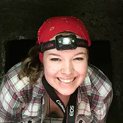 Woman wearing a headlamp with camera strap around her neck.